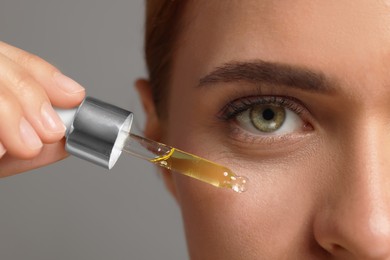 Beautiful young woman applying cosmetic serum onto her face on grey background, closeup