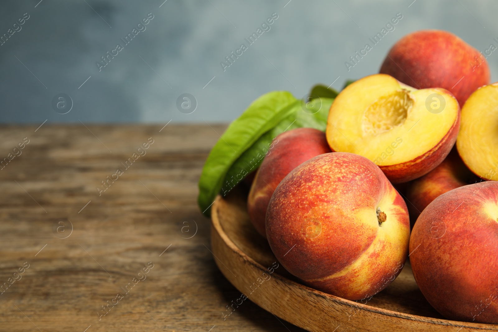 Photo of Plate with fresh peaches and leaves on wooden table, space for text