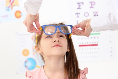 Photo of Female ophthalmologist putting glasses on little girl in clinic