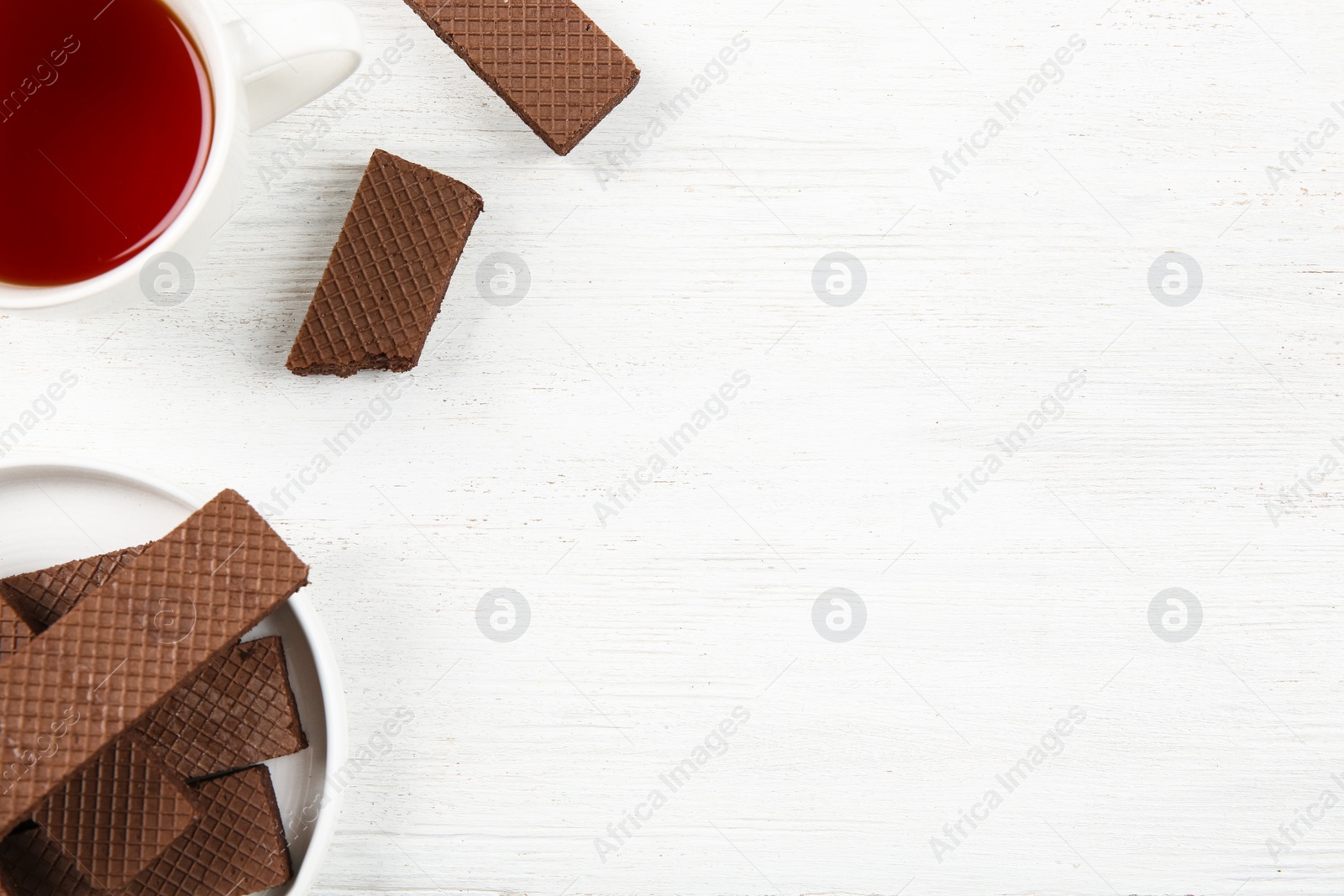 Photo of Plate of delicious chocolate wafers with cup of tea on white wooden background, top view. Space for text