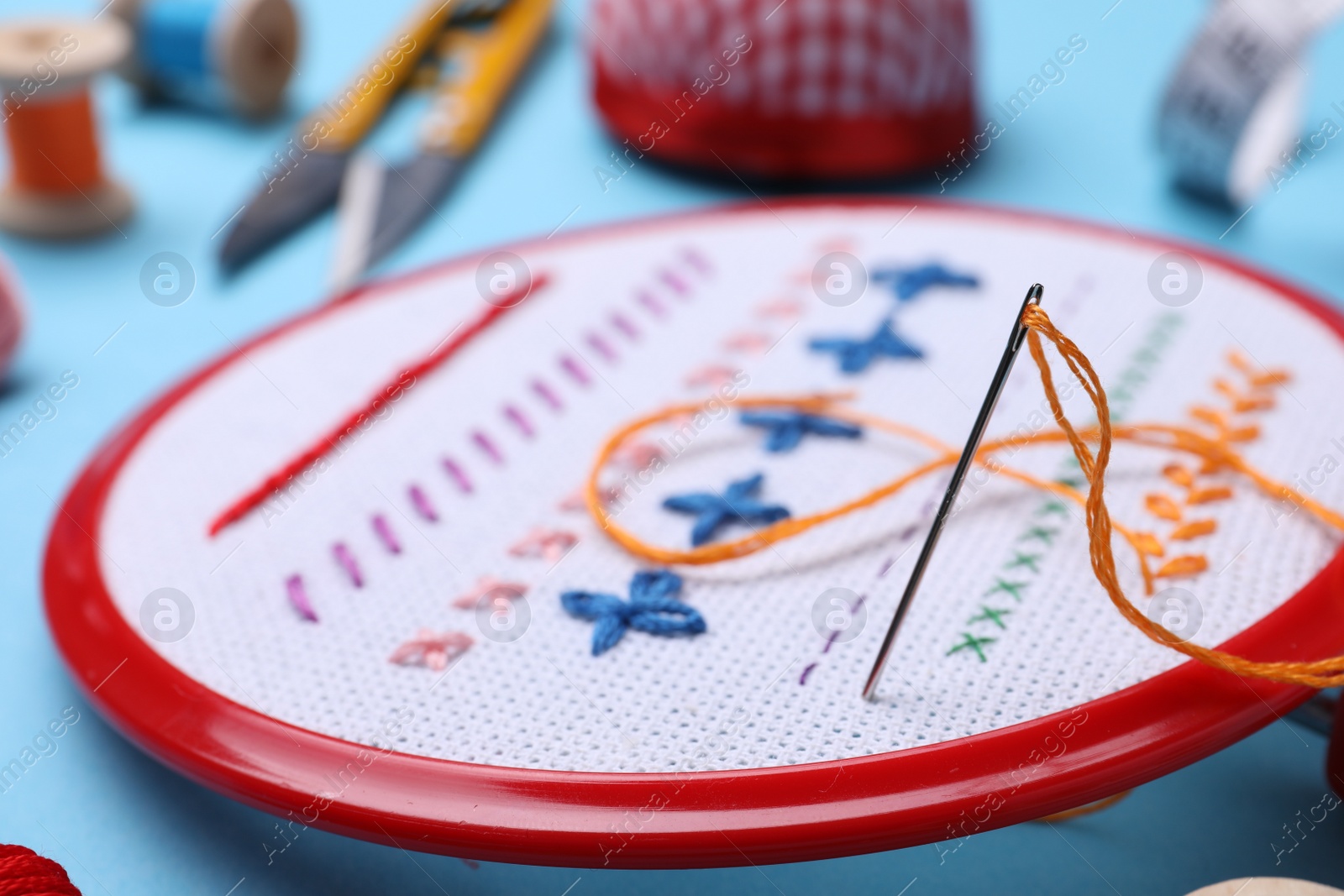 Photo of Embroidery hoop with fabric and needle on light blue background, closeup