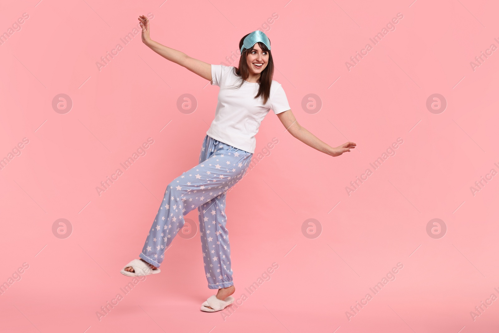 Photo of Happy woman in pyjama and sleep mask on pink background