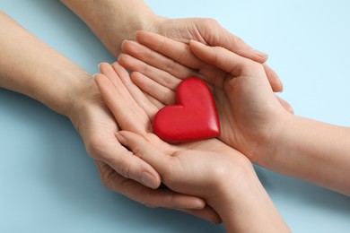 Photo of Young and elderly women holding red heart on light blue background, closeup