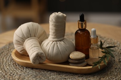 Photo of Spa composition. Herbal sacks, cosmetic products and stones on table indoors, closeup