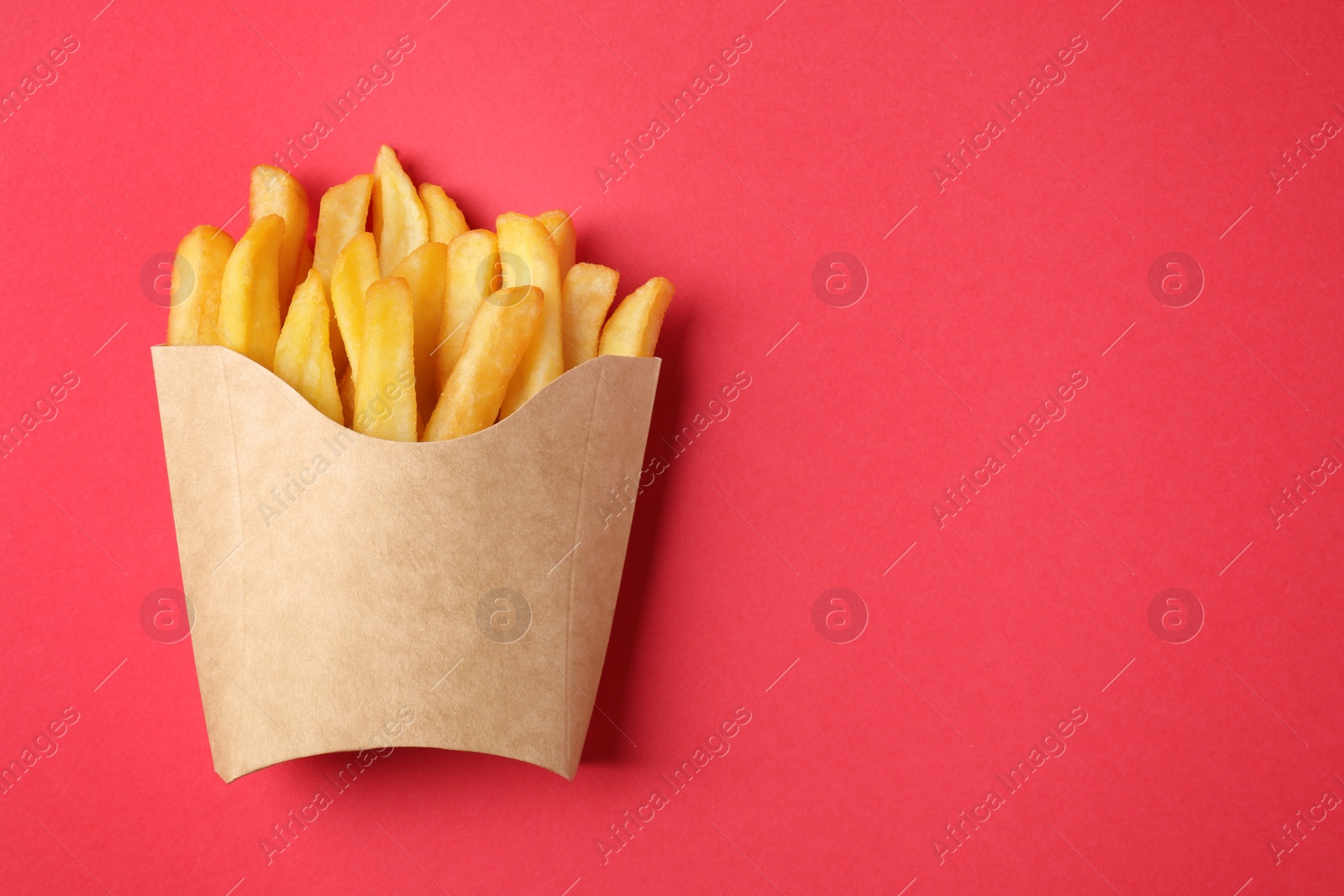 Photo of Paper cup with French fries on red table, top view. Space for text