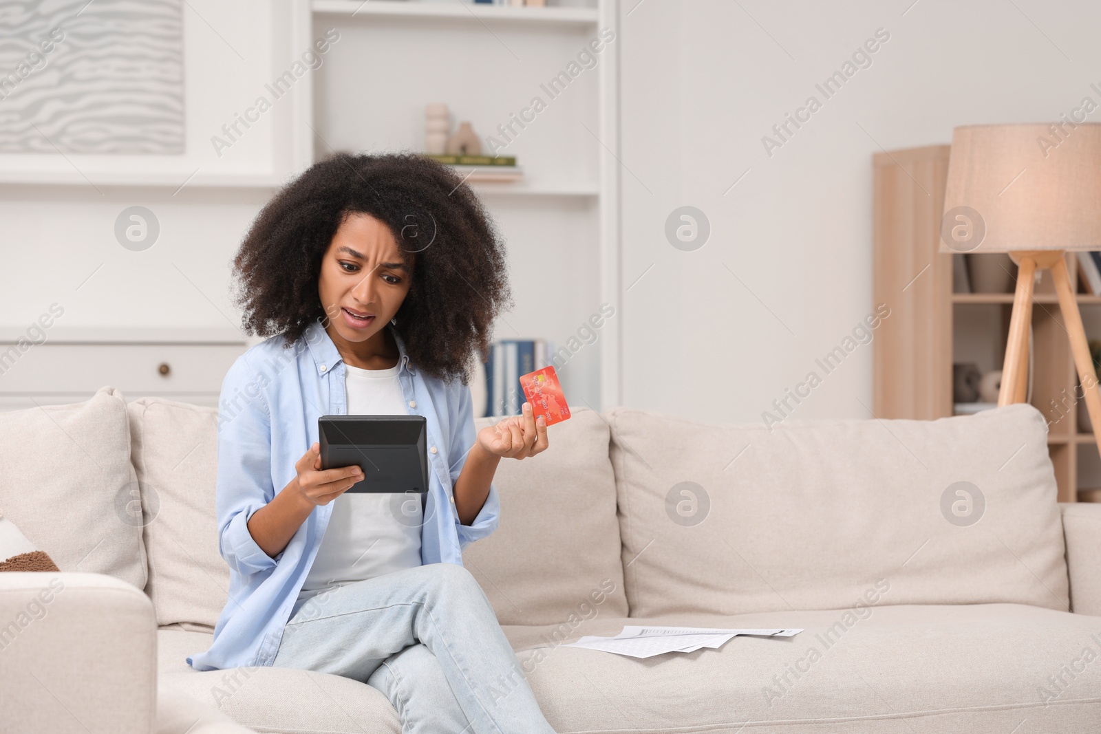Photo of Shocked woman with calculator and credit card planning budget at home. Debt problem
