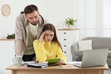 Photo of Young couple discussing family budget at table in living room