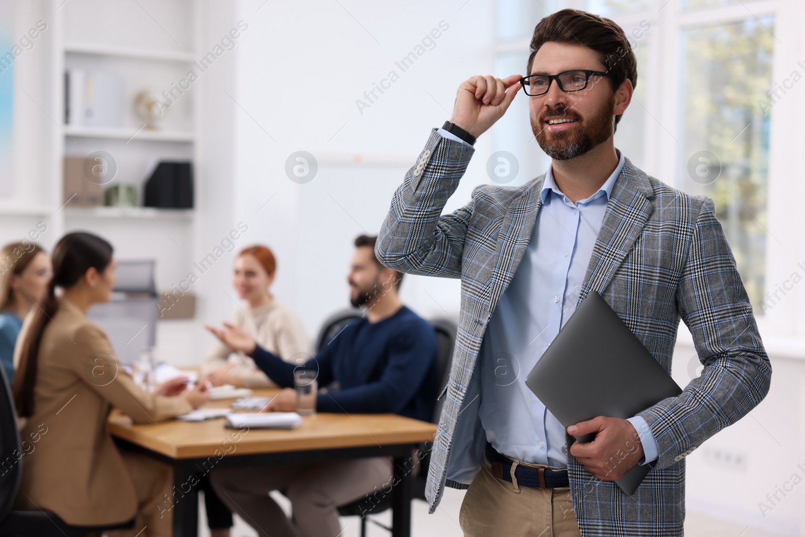 Photo of Team of employees working together in office. Stylish businessman with laptop indoors