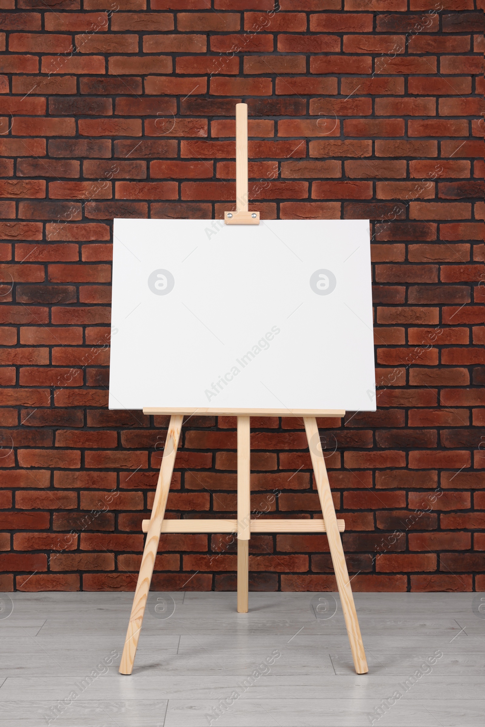 Photo of Wooden easel with blank canvas near brick wall indoors