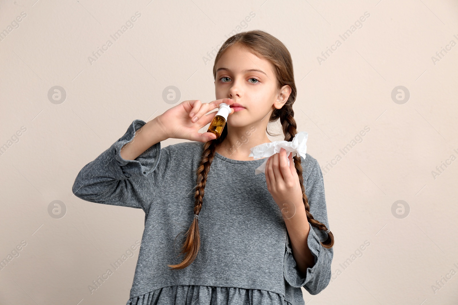 Photo of Sick little girl using nasal spray on beige background