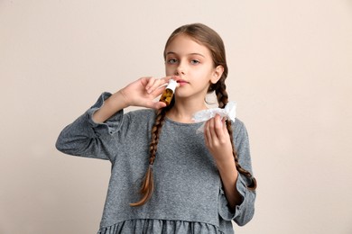 Sick little girl using nasal spray on beige background