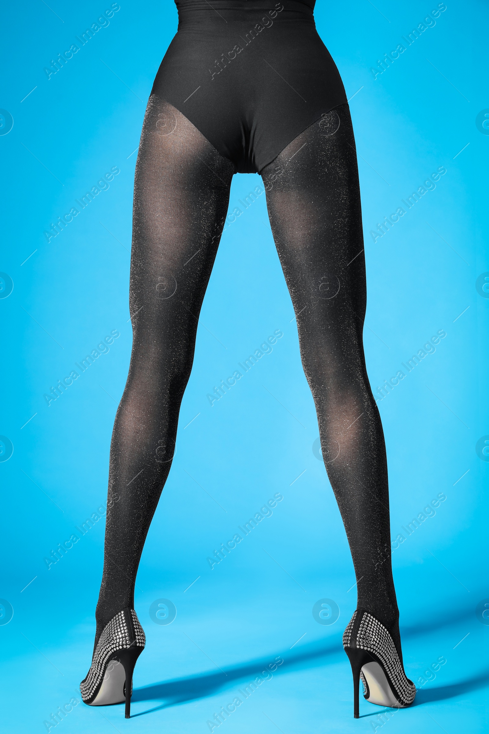 Photo of Woman wearing black tights and stylish shoes on blue background, closeup of legs