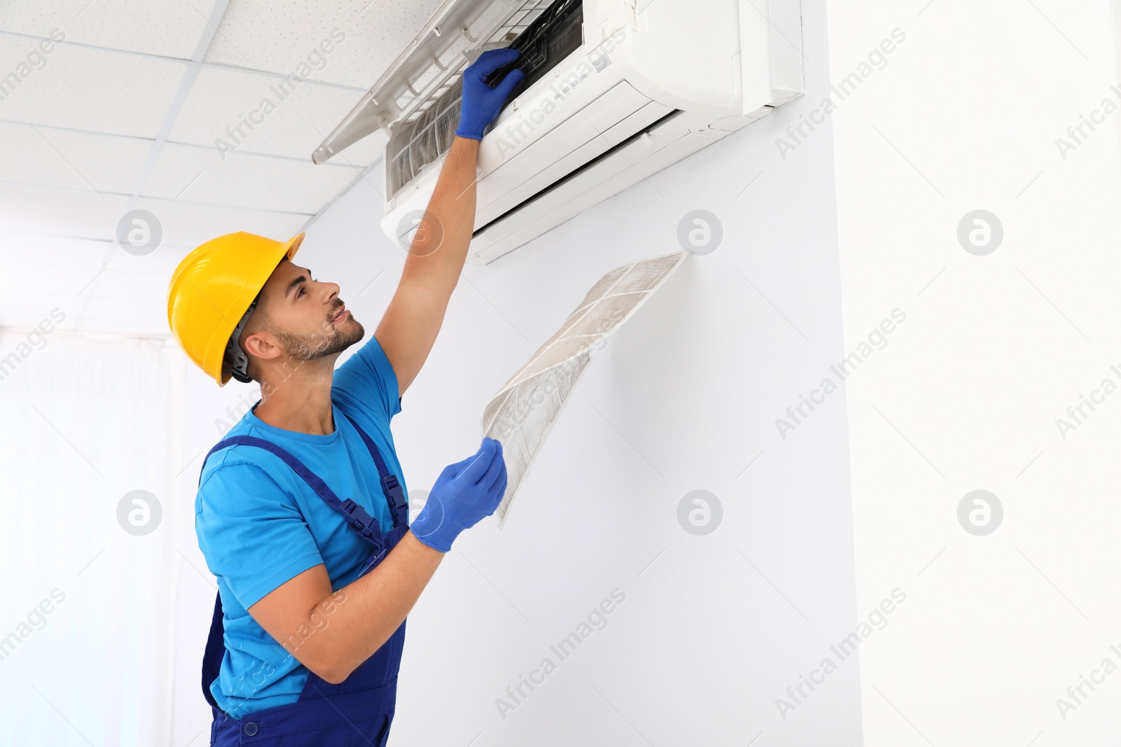 Photo of Professional technician maintaining modern air conditioner indoors