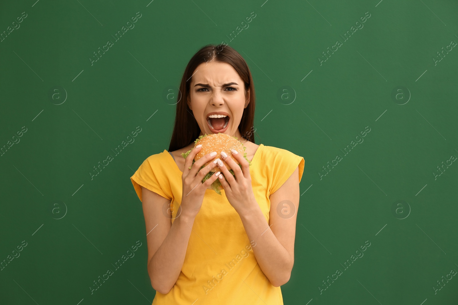 Photo of Young woman eating tasty burger on color background