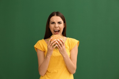 Photo of Young woman eating tasty burger on color background
