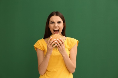 Young woman eating tasty burger on color background