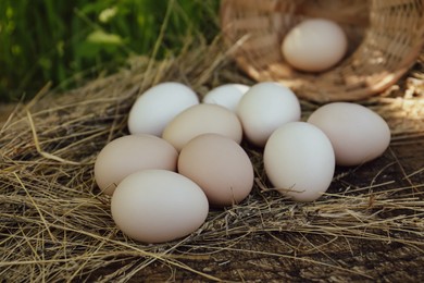 Photo of Fresh raw eggs and straw on wooden surface outdoors, closeup