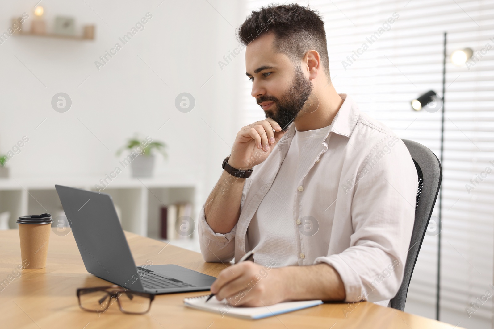 Photo of Young man watching webinar at table in room