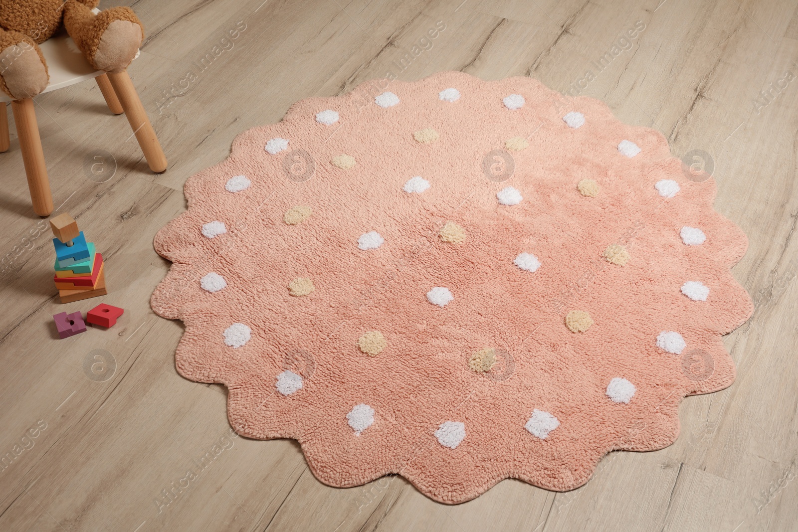 Photo of Round pink rug with polka dot pattern and toys on wooden floor in baby's room