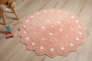 Photo of Round pink rug with polka dot pattern and toys on wooden floor in baby's room