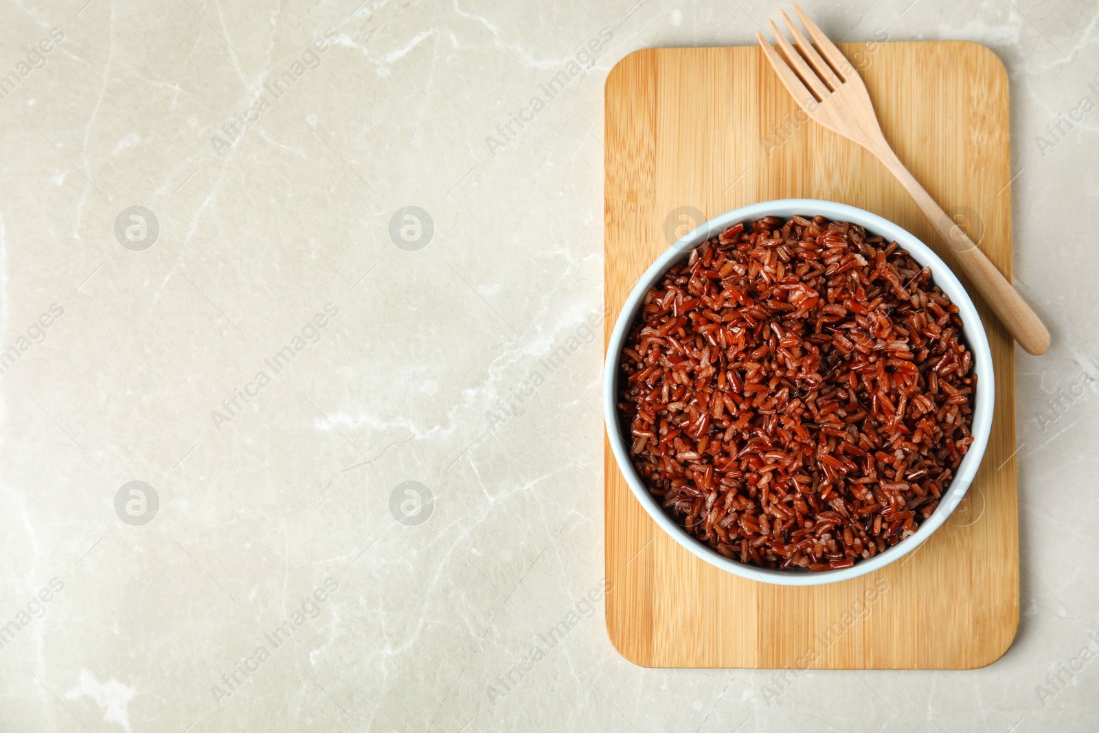 Photo of Bowl with delicious cooked brown rice on white marble table, top view. Space for text