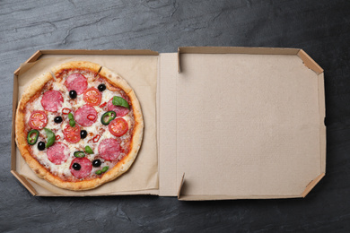 Photo of Delicious pizza Diablo  in cardboard box on dark background, top view
