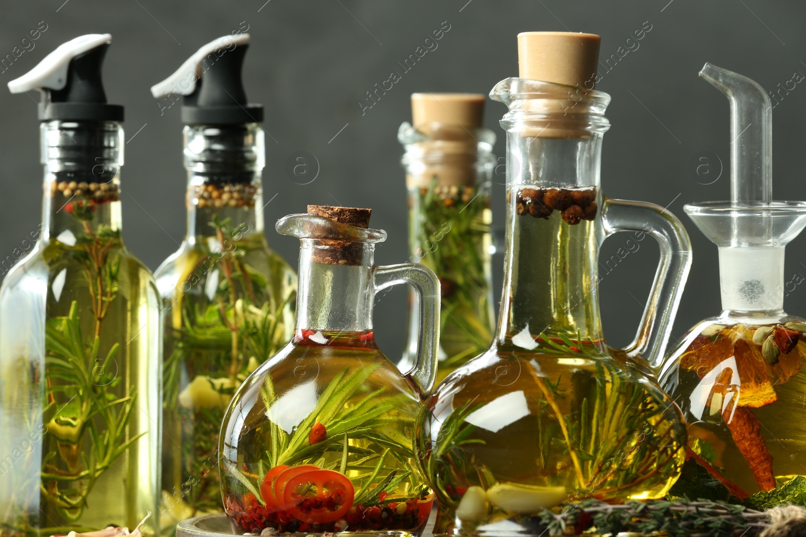 Photo of Cooking oil with different spices and herbs in bottles against grey background