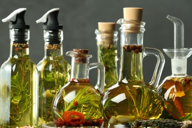Photo of Cooking oil with different spices and herbs in bottles against grey background