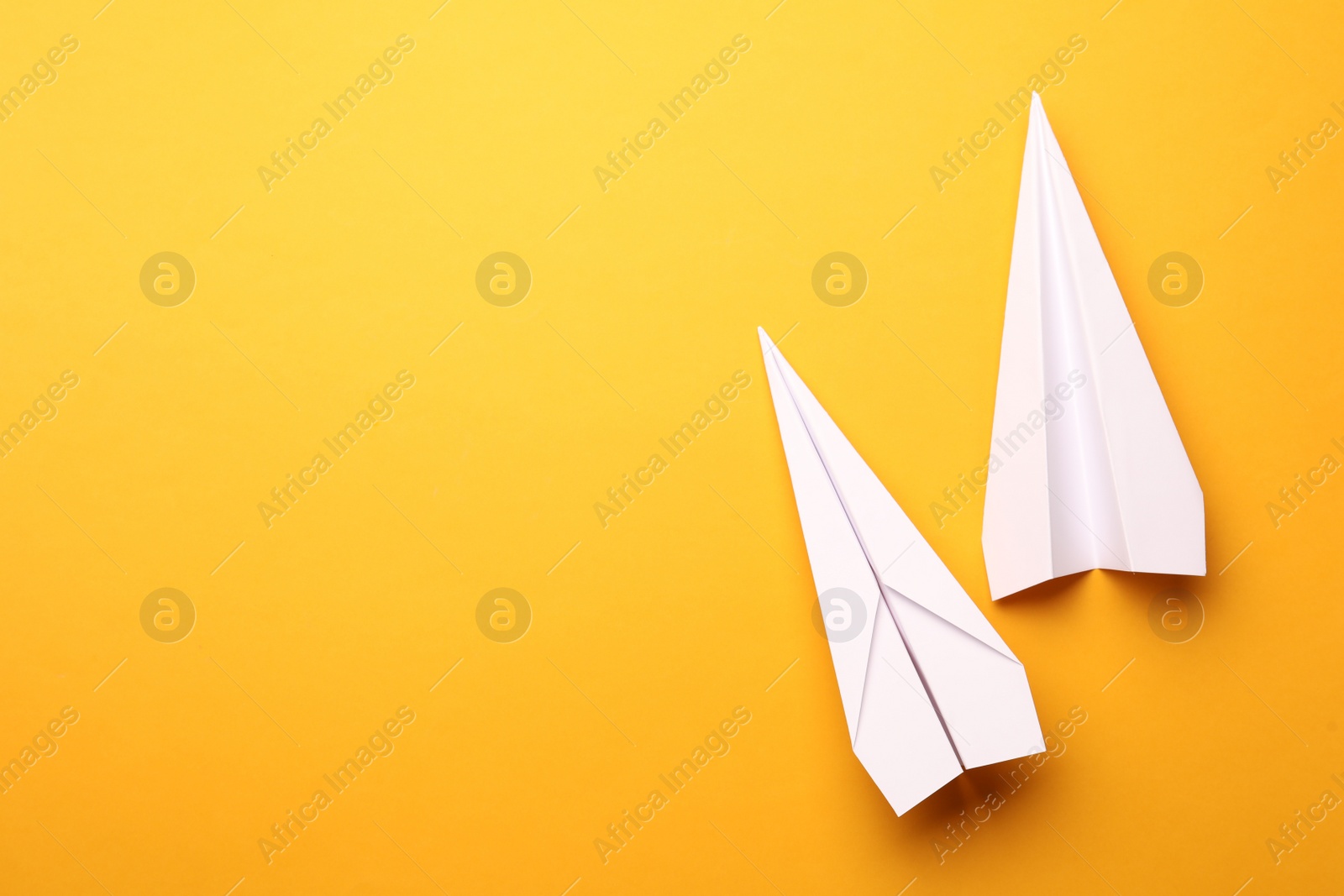 Photo of Handmade white paper planes on yellow background, flat lay. Space for text