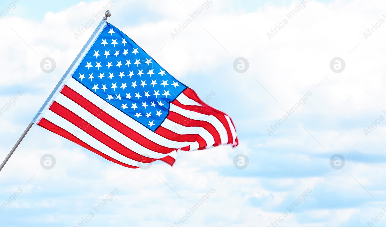 Photo of American flag near river on cloudy day. Space for text