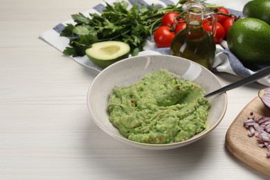 Preparing delicious guacamole in bowl and ingredients on white wooden table