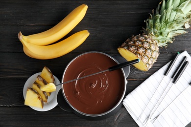 Flat lay composition with chocolate fondue in pot and fruits on wooden background