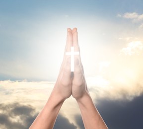 Image of Religion. Christian woman with glowing cross praying against sky, closeup