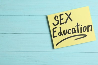 Photo of Note with phrase "SEX EDUCATION" on light blue wooden background, top view. Space for text