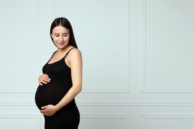 Beautiful pregnant woman in black dress near light grey wall, space for text