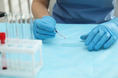 Doctor with blood sample from finger at table in laboratory, closeup