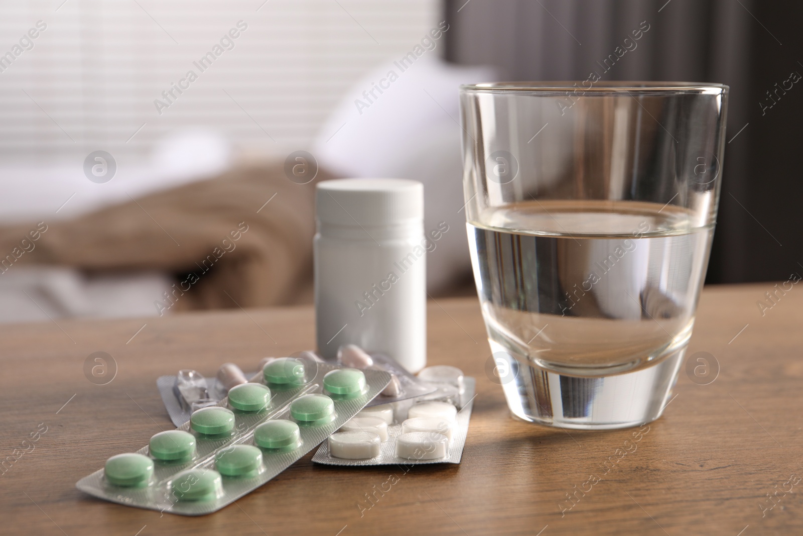 Photo of Glass of water, different pills in blisters and medical bottle on wooden table indoors. Space for text