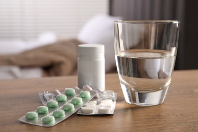 Photo of Glass of water, different pills in blisters and medical bottle on wooden table indoors. Space for text