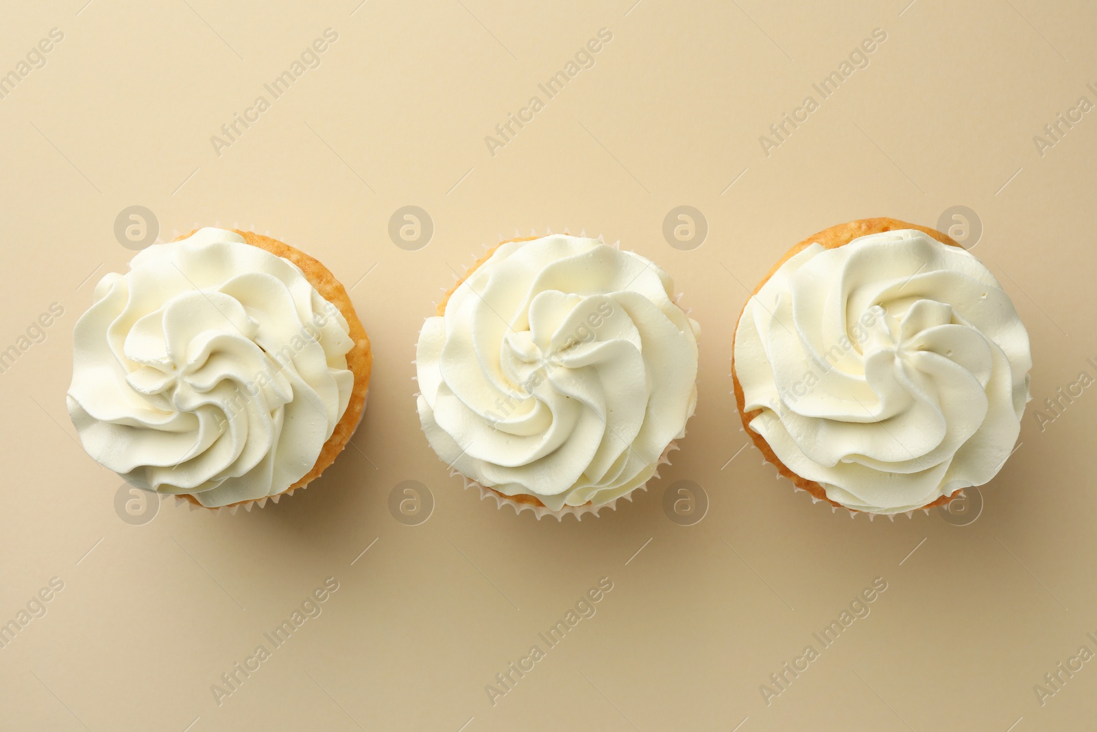 Photo of Tasty vanilla cupcakes with cream on beige background, top view