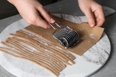 Photo of Woman making soba (buckwheat noodles) with cutter at grey table, closeup