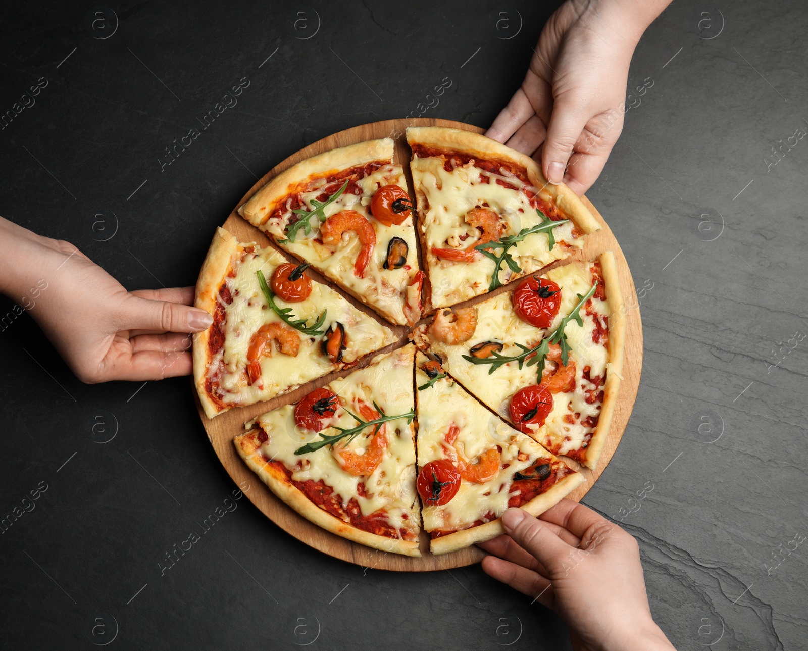 Photo of People taking pieces of delicious seafood pizza at black table, top view