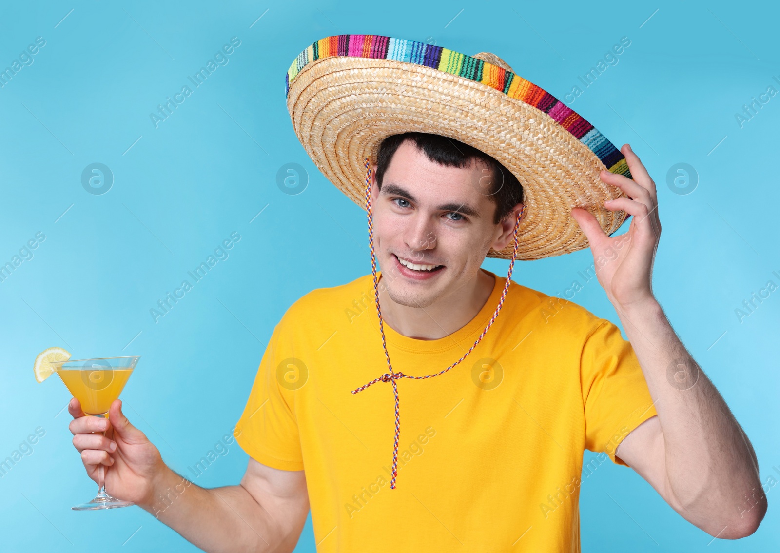 Photo of Young man in Mexican sombrero hat with cocktail on light blue background