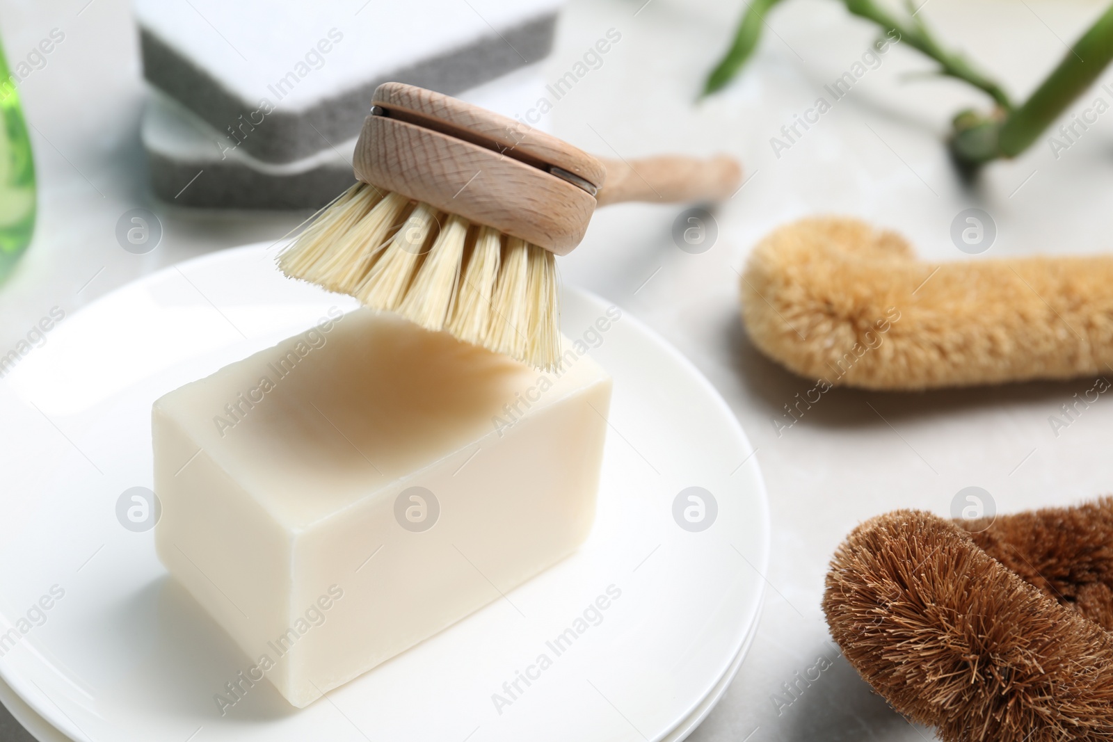 Photo of Cleaning brushes, soap bar and plates on table, closeup. Dish washing supplies