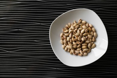 Many tasty pistachios on black table, top view. Space for text