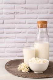 Tasty fresh milk and cottage cheese on table against white brick wall. Space for text