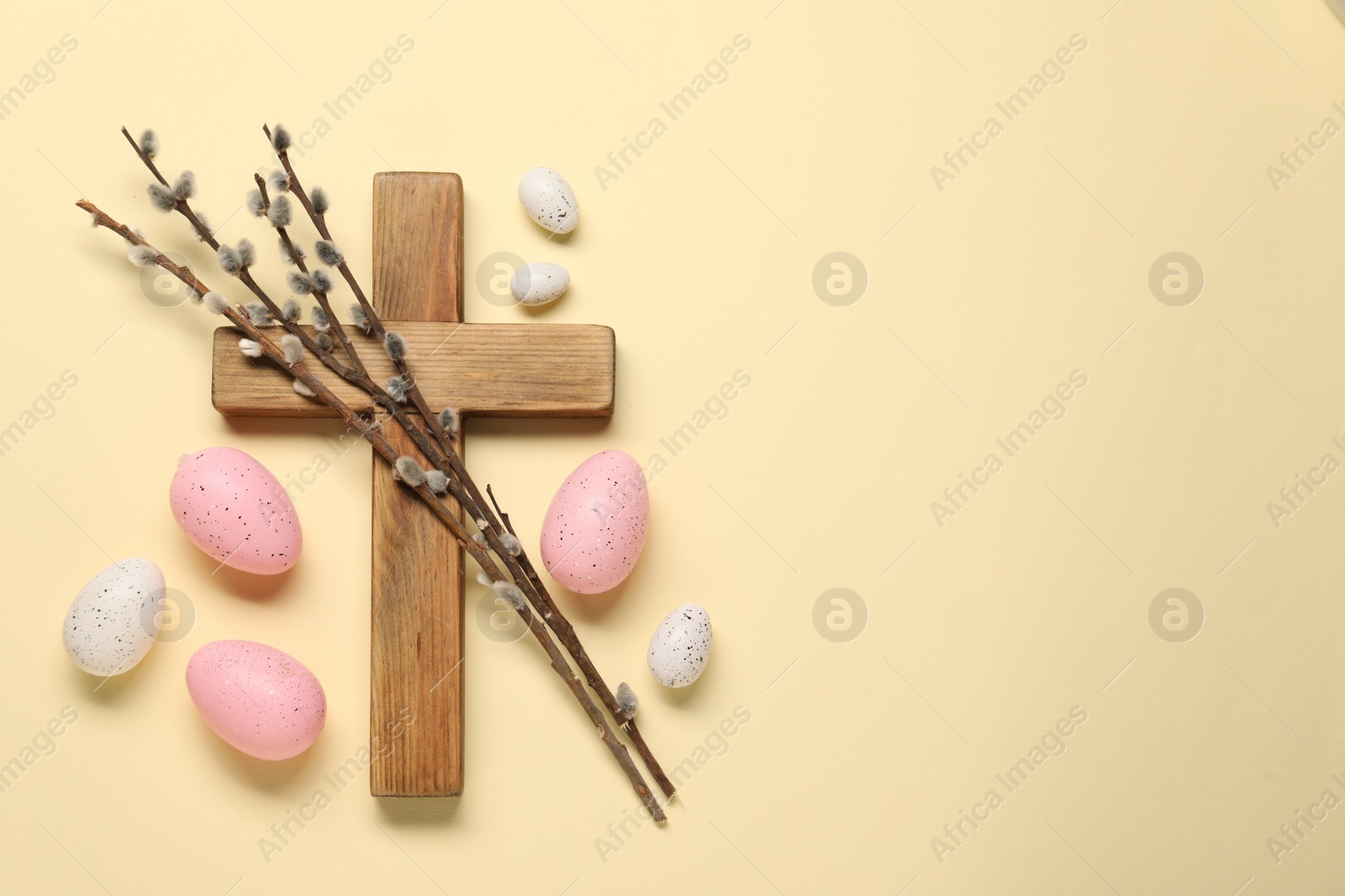 Photo of Wooden cross, painted Easter eggs and willow branches on beige background, flat lay. Space for text