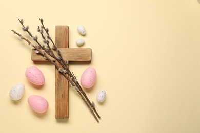 Wooden cross, painted Easter eggs and willow branches on beige background, flat lay. Space for text