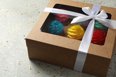 Box with delicious colorful cupcakes and confetti on light grey table