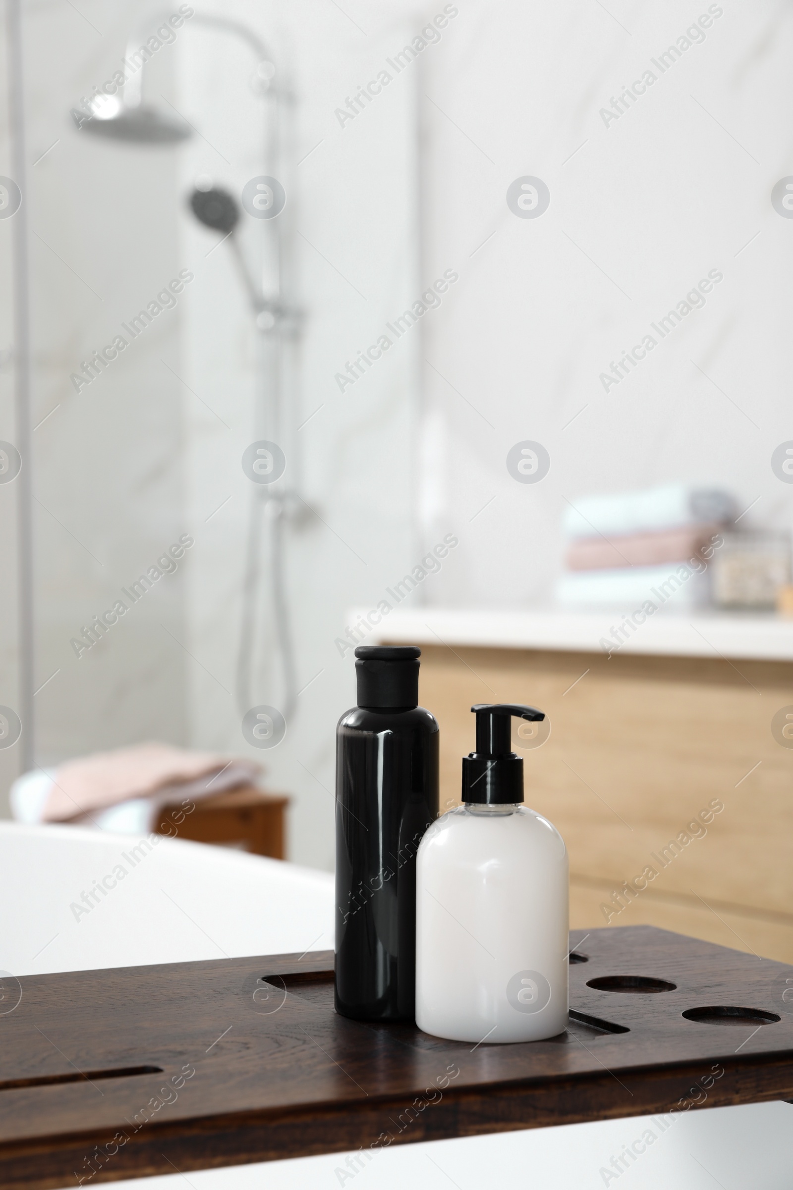 Photo of Wooden bath tray with bottles of shower gels on tub indoors