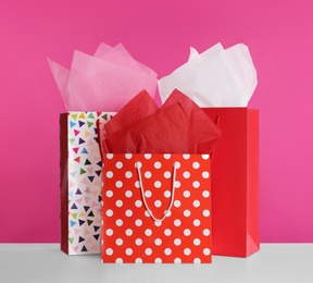 Photo of Gift bags with paper on white table against pink background